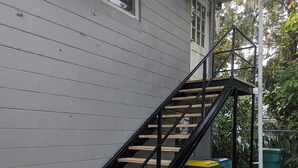 A staircase with wooden steps and black metal railings leading to a house with gray siding. - Charming, treetop Indian River Hideaway (Cocoa)