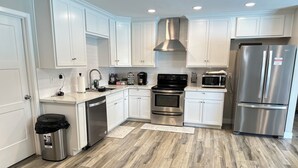 A modern kitchen with white cabinets, stainless steel appliances, and a herringbone wood floor. - A Getaway Home with a pool table, table tennis & a Pool. (Phoenix)