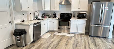 A modern kitchen with white cabinets, stainless steel appliances, and a herringbone wood floor.