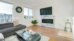 A modern living room with a grey sofa, a glass coffee table, a fireplace, and a TV mounted above it. - Elegant Home In Victoria BC (Langford)