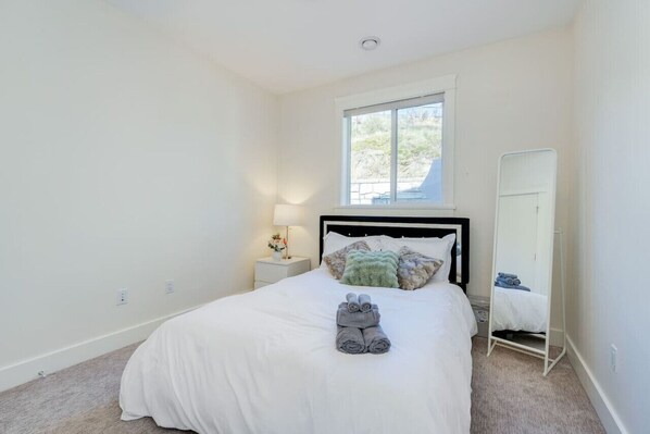 A bedroom with a bed, a nightstand with a lamp, a window, and a wardrobe.
