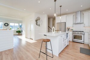A modern kitchen with white cabinetry, a central island with a bar stool, a stove, and pendant lighting.
