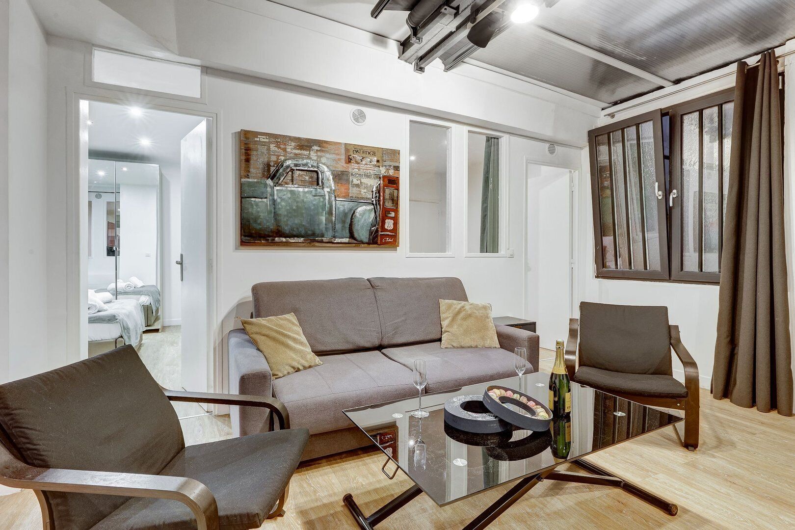 Uma sala de estar moderna com um sofá cinzento, duas poltronas, uma mesa de centro de vidro e um quadro na parede.