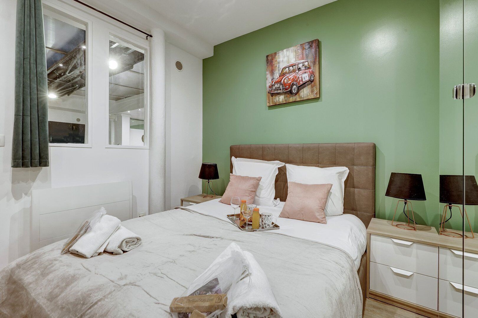 Cama bem arrumada com travesseiros, mesa de cabeceira com abajur e um quadro na parede.