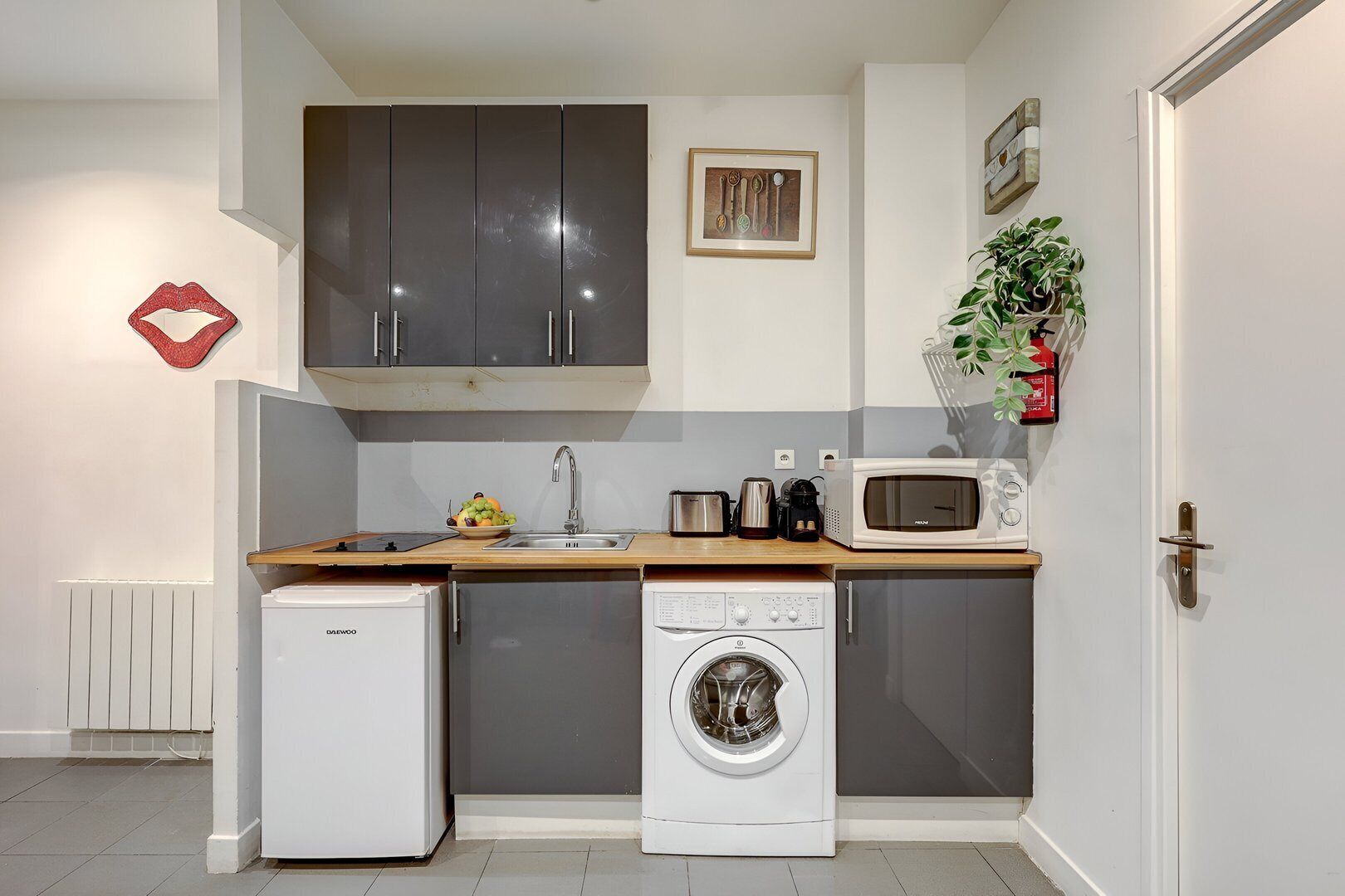 A compact kitchen with a refrigerator, washing machine, microwave, and sink.