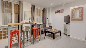 Un espacio habitable compacto con zona de comedor, sofá, mesa de centro y televisión.