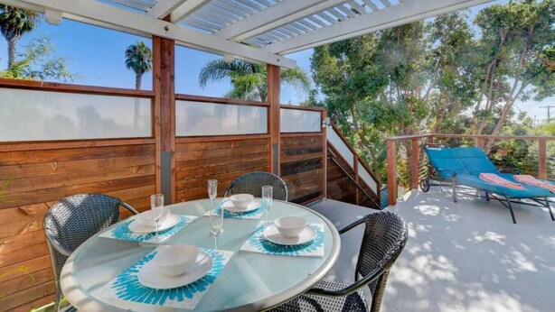 A covered outdoor patio with a table set for dining, chairs, and a lounge area with a blue cushion.