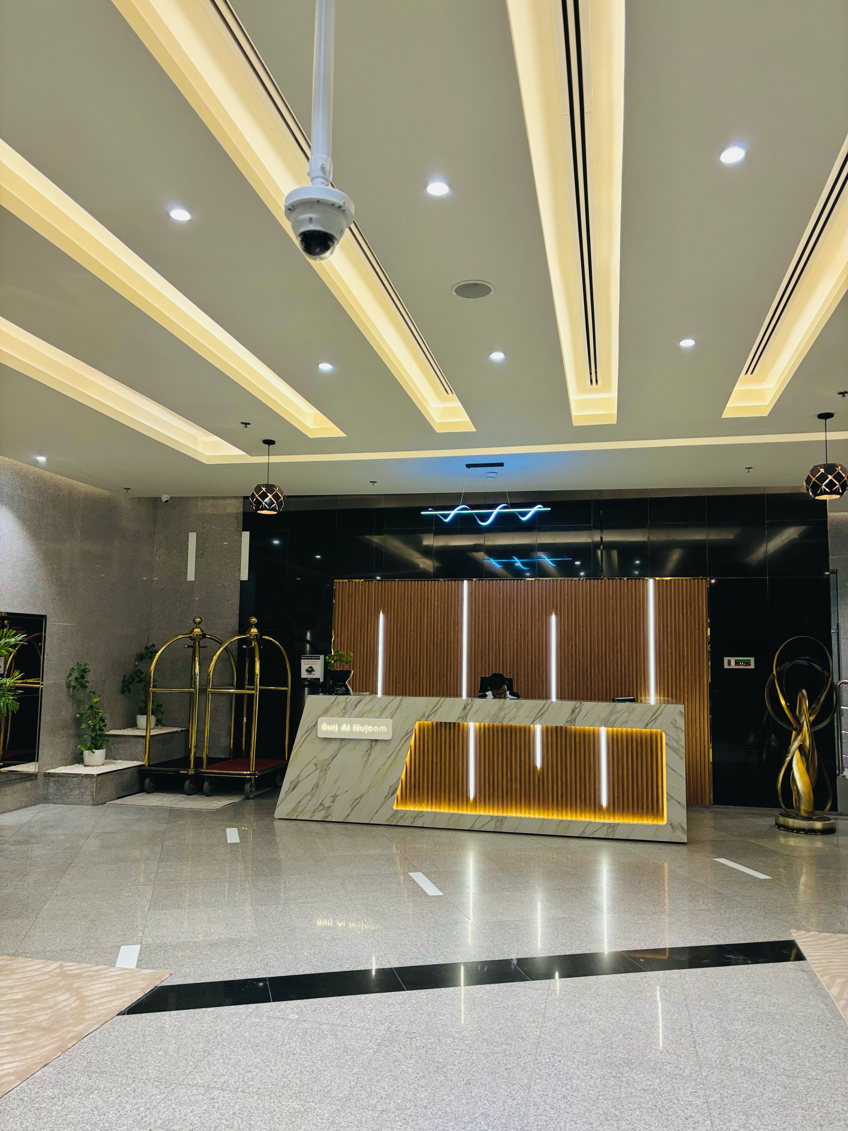 Un espace d’accueil moderne avec un comptoir en marbre, des luminaires au plafond et une caméra de surveillance.