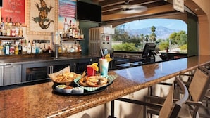 A bar area with a granite countertop, bar stools, and a view of mountains through a large window. - Marriott Shadow Ridge Studio Unit- full resort access - Perfect for Coachella (Palm Desert)