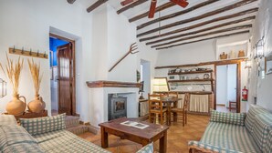 Una sala de estar acogedora con chimenea, sofás a cuadros, una mesa de madera y una zona de cocina al fondo.