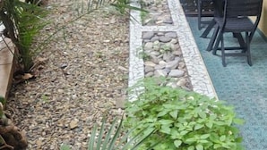 A garden with a tiled pathway, potted plants, and outdoor furniture.