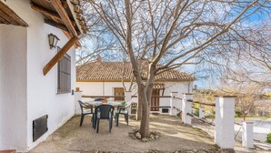 A patio with a table and chairs, a tree, and a white building with a tiled roof.