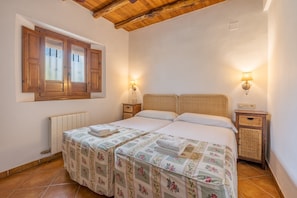 Ein Doppelbett mit Blumenmuster, zwei Nachttische inklusive Lampen, eine Holzbalkendecke und ein Fenster mit Rollläden.