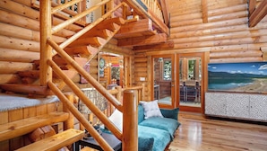 L’intérieur d’une cabane en rondins, avec un escalier en bois, un canapé bleu et une grande fenêtre donnant sur un paysage pittoresque.