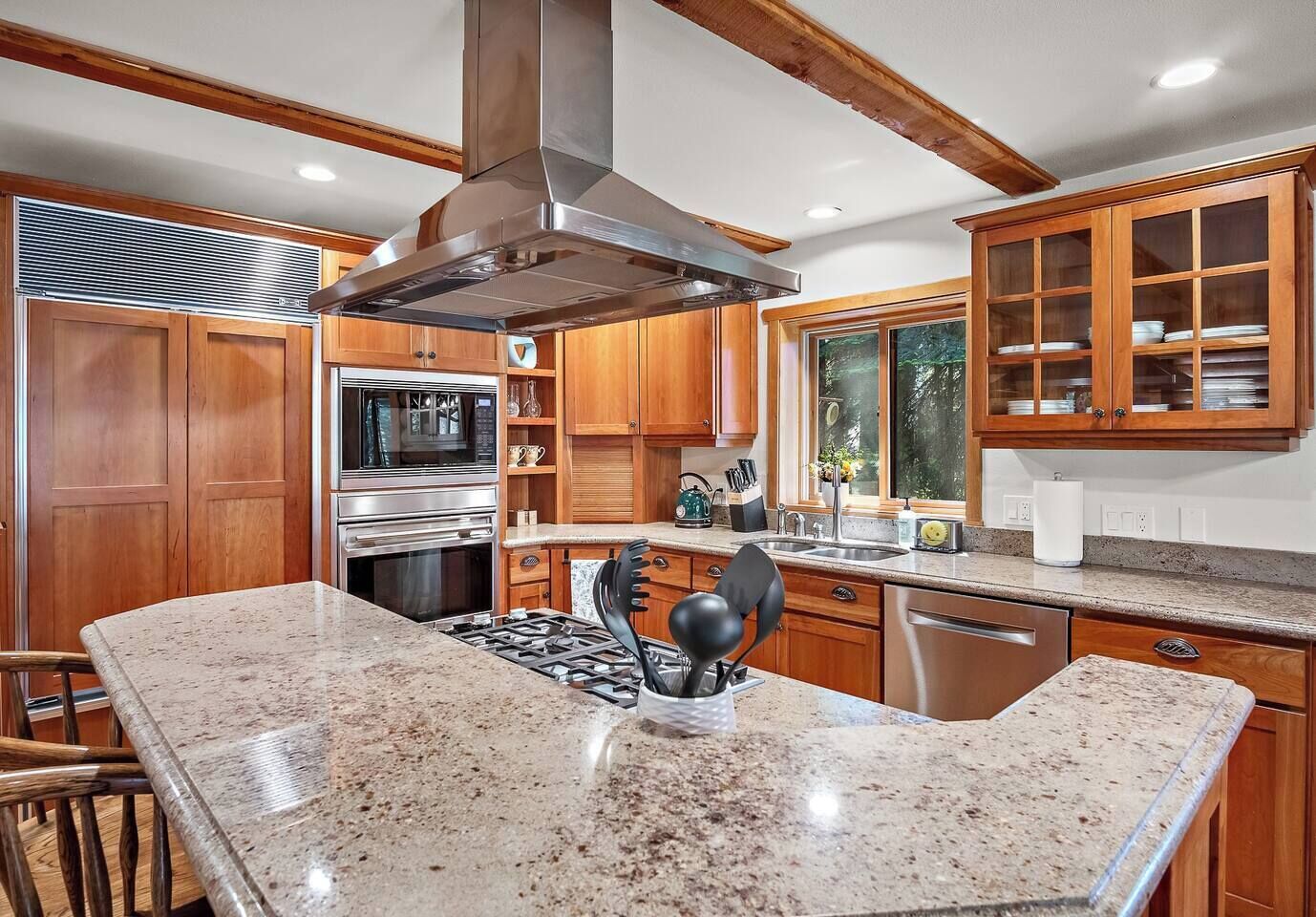 A kitchen with wooden cabinets, stainless steel appliances, granite countertops, and a large window.