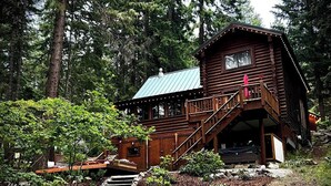 Une cabane en bois avec un escalier menant à une terrasse, le tout entouré d’arbres.