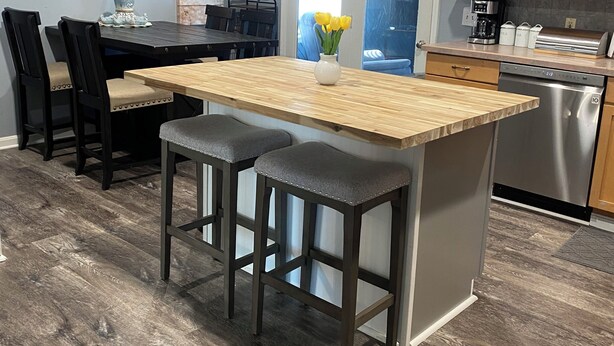 A modern kitchen with a central island, bar stools, wooden cabinets, and a dining area with chairs.