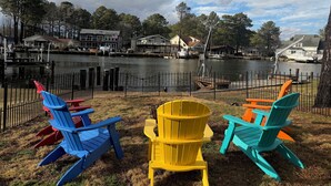 A lakeside view with colorful Adirondack chairs, a dock, and houses in the background.