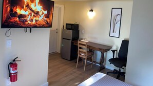 A room with a television displaying a fire, a microwave, a refrigerator, a wooden desk, a chair, and a fire extinguisher. - Blue Door at Lake Serene (Lynnwood)