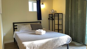 A neatly made bed with a white duvet, a bedside table with a lamp, a window with curtains, and a wooden floor. - Blue Door at Lake Serene (Lynnwood)