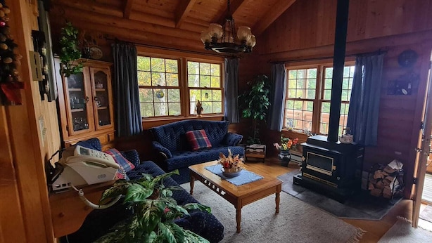 A cozy cabin interior with a wooden interior, a sofa, a coffee table, a fireplace, and a view of the outdoors. - Cozy log cabin with fantastic views and 2 bathrooms (The Points West Bay)