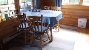 A wooden cabin interior with a dining table, chairs, and a window with curtains. - Cozy log cabin with fantastic views and 2 bathrooms (The Points West Bay)