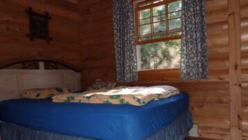 A wooden cabin bedroom with a bed, curtains, and a window.