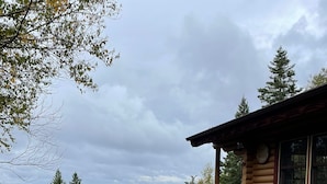A log cabin with a wooden staircase leading to a porch, surrounded by a gravel driveway and a view of a lake and forest. - Cozy log cabin with fantastic views and 2 bathrooms (The Points West Bay)
