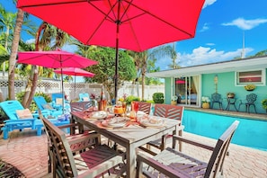 A poolside dining area with a table set for four, surrounded by blue lounge chairs and red umbrellas.