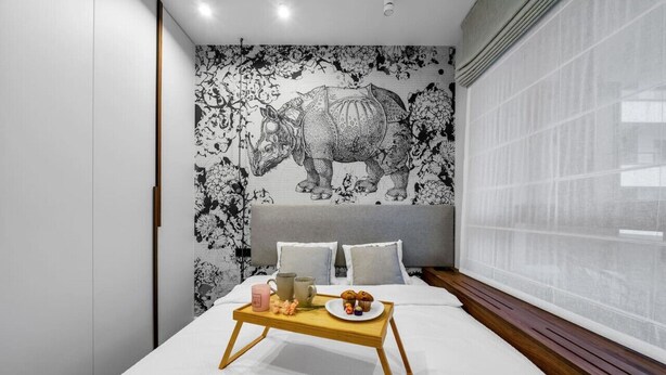 A bedroom with a large bed, a tray with breakfast items, and a wall mural of a rhinoceros. - Warsaw Postępu Apartment - Parking, Balcony, A/C - by Rentujemy (Warszawa)