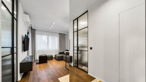 A modern living room with a sectional sofa, a flat-screen TV, and a large sliding glass door leading to a balcony. - Warsaw Postępu Apartment - Parking, Balcony, A/C - by Rentujemy (Warszawa)