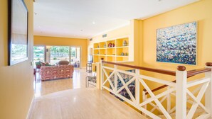 A spacious living area with a wooden staircase, a balcony with outdoor furniture, and a bookshelf with decorative items.