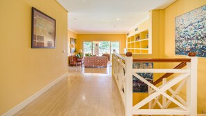 A spacious hallway with a wooden floor leading to a living area with a sofa and chairs.