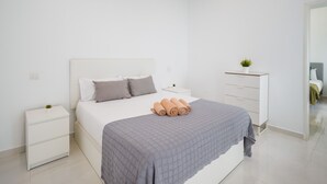 A modern bedroom with a bed, a nightstand, a dresser, and a small potted plant. - Confital Beach Home  By CanariasGetaway (Las Palmas de Gran Canaria)