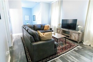 Un salon avec un canapé d’angle, un téléviseur posé sur un meuble en bois et un tapis à motifs.