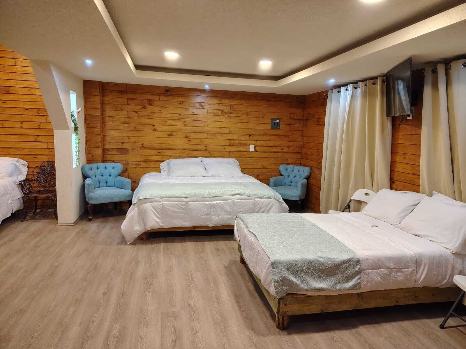 A room with three beds, wooden walls, and a TV on the wall.