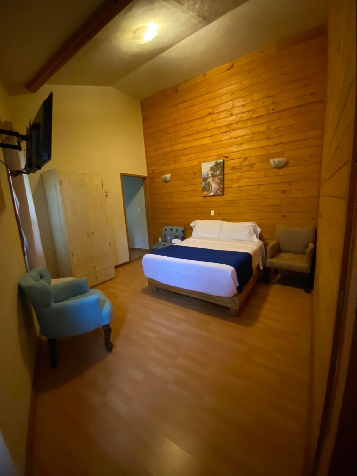 A bedroom with a wooden wall, a bed, a chair, and a cabinet.