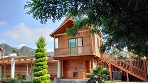 A wooden two-story building with a balcony, a staircase, and a garden with benches. -  Hotel Cabaña iilldaa, Malinalco (Malinalco)