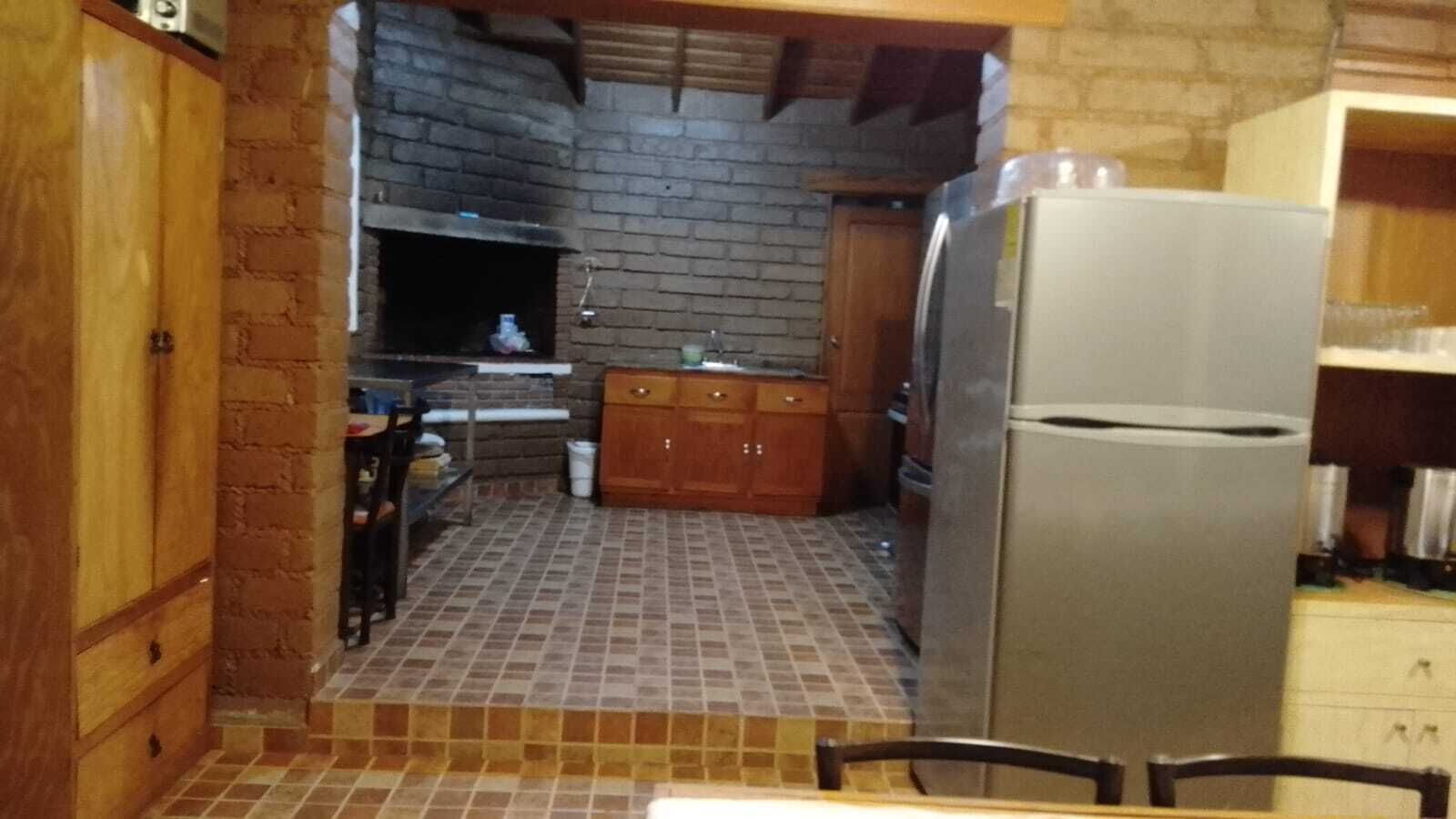 A compact kitchen with a tiled floor, a refrigerator, wooden cabinets, and a brick wall.