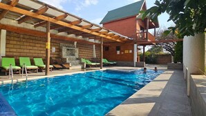 A swimming pool with green lounge chairs and a wooden pergola overhead. -  Hotel Cabaña iilldaa, Malinalco (Malinalco)