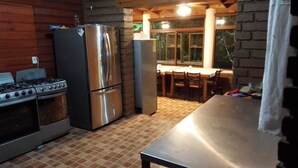 A kitchen with a stove, refrigerator, and dining area with chairs and a table. -  Hotel Cabaña iilldaa, Malinalco (Malinalco)