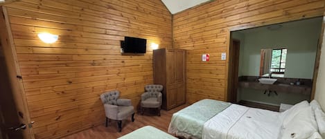 Habitación con paredes de madera, dos camas, ventilador de techo, televisión, armario y espejo con lavabo.