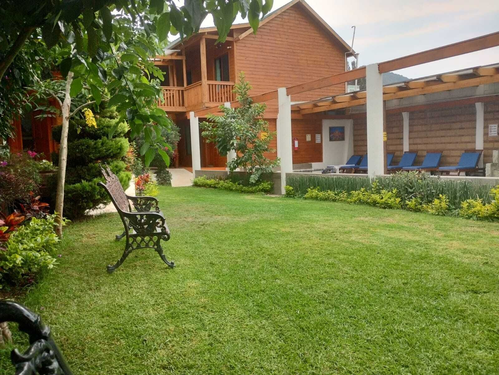 A wooden house with a covered patio area, a lawn, and a seating area with blue chairs.