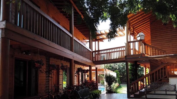 A wooden covered outdoor area with a staircase leading to a second level, surrounded by potted plants and a view of a garden. -  Hotel Cabaña iilldaa, Malinalco (Malinalco)