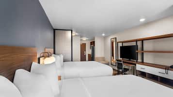 A modern hotel room with a large bed, a desk with a computer, a TV, and a seating area with a chair and a sofa.