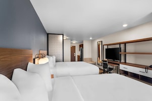 Una habitación de hotel moderna con una cama grande, un escritorio con computadora, televisor y una zona de estar con una silla y un sofá.