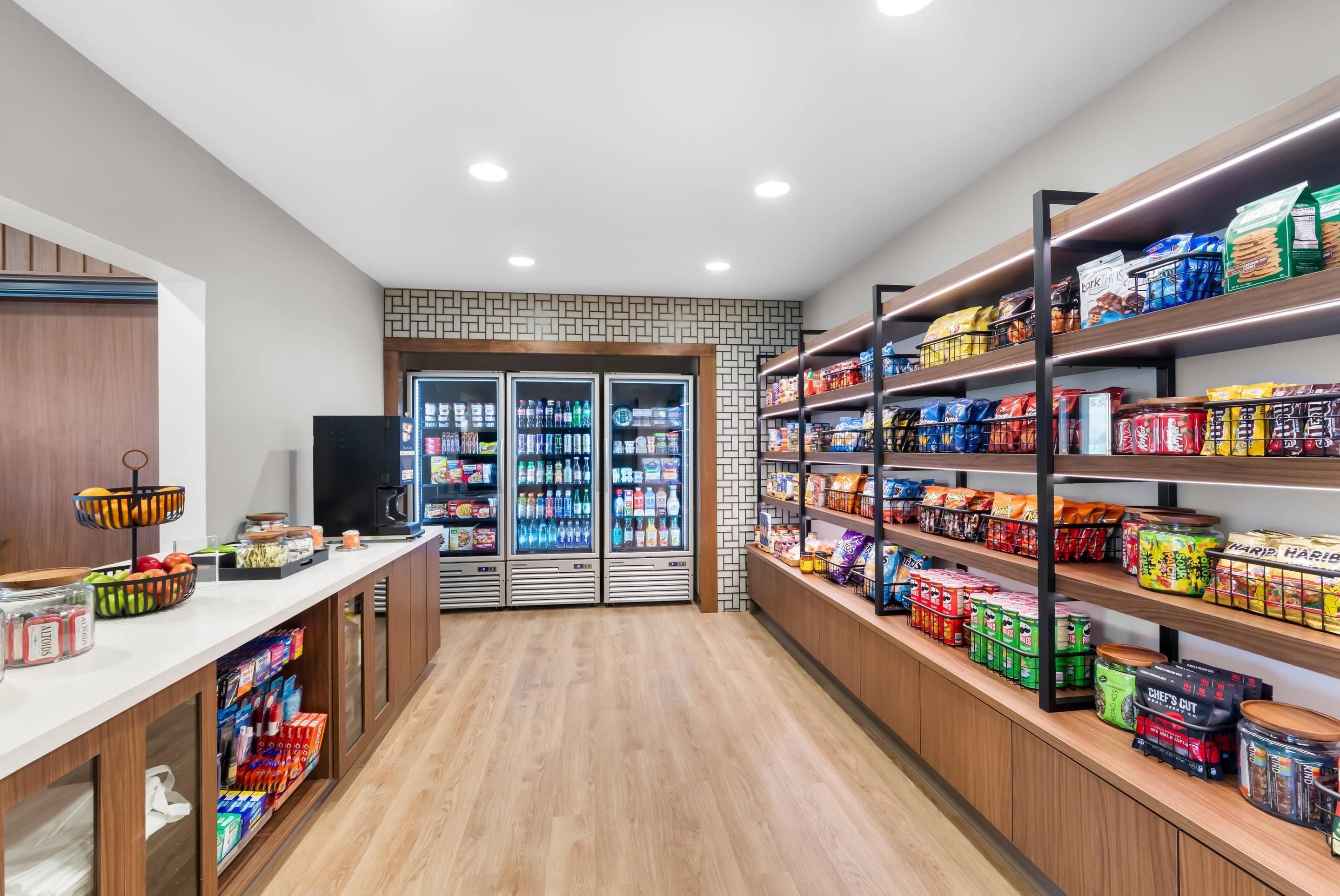 A well-lit, modern food service area with refrigerated display cases, shelves stocked with snacks, and a clean, wooden floor.