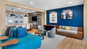 A modern living room with a blue accent wall, a sofa, a coffee table, and a TV. - Everhome Suites Bastrop By Choice Hotels (Bastrop)
