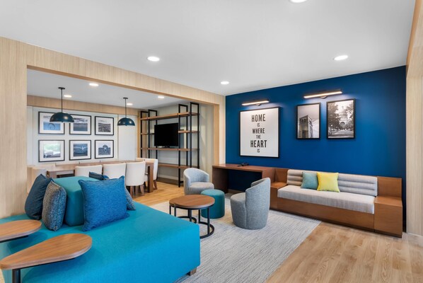 A modern living room with a blue accent wall, a sofa, a coffee table, and a TV. - Everhome Suites Bastrop By Choice Hotels (Bastrop)