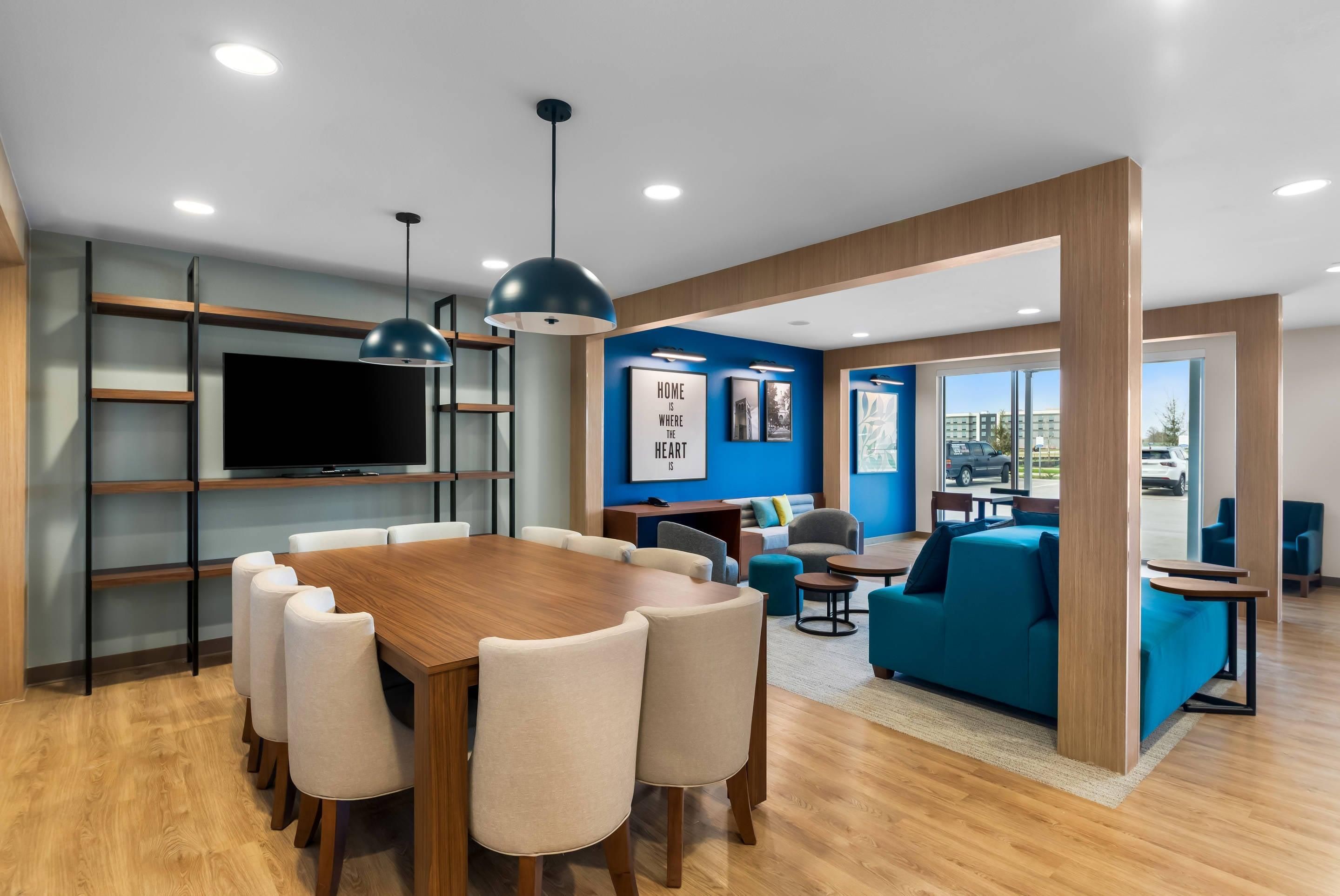 A modern interior with a wooden dining table, chairs, a TV, and a blue accent wall.